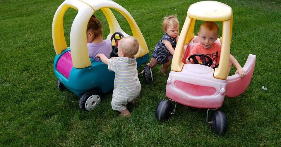 Three children playing with two toy cars on grass