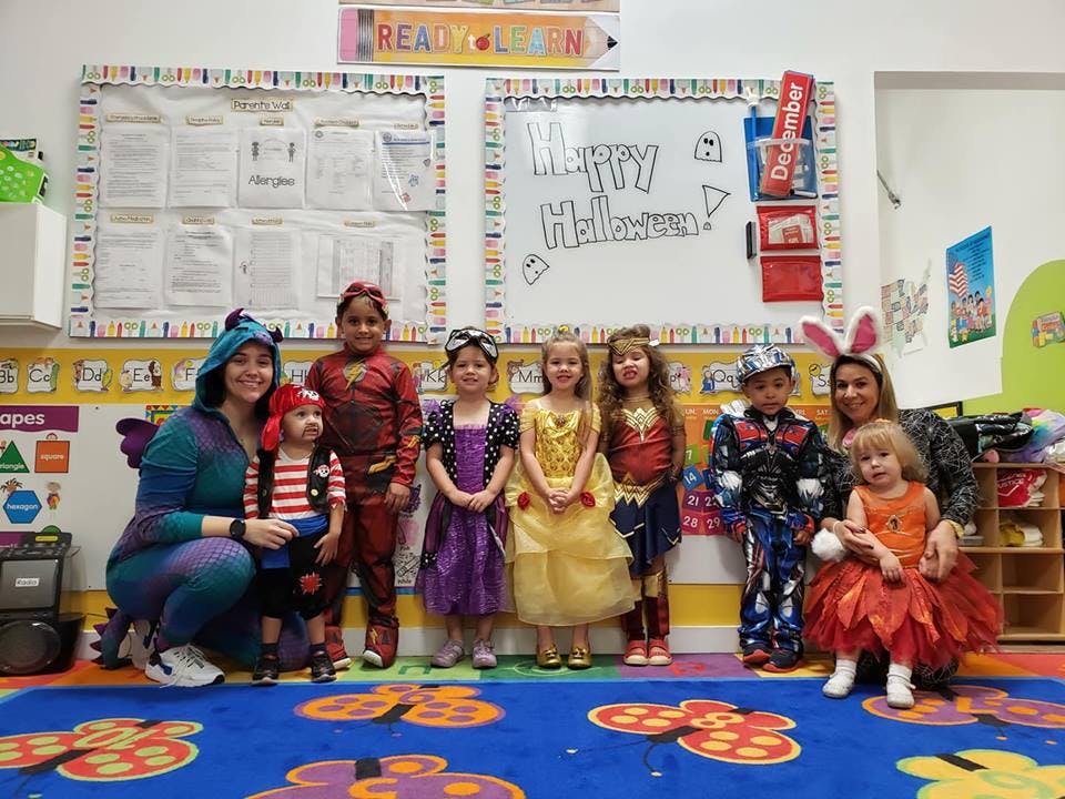 Two people and seven children in costumes standing in a classroom