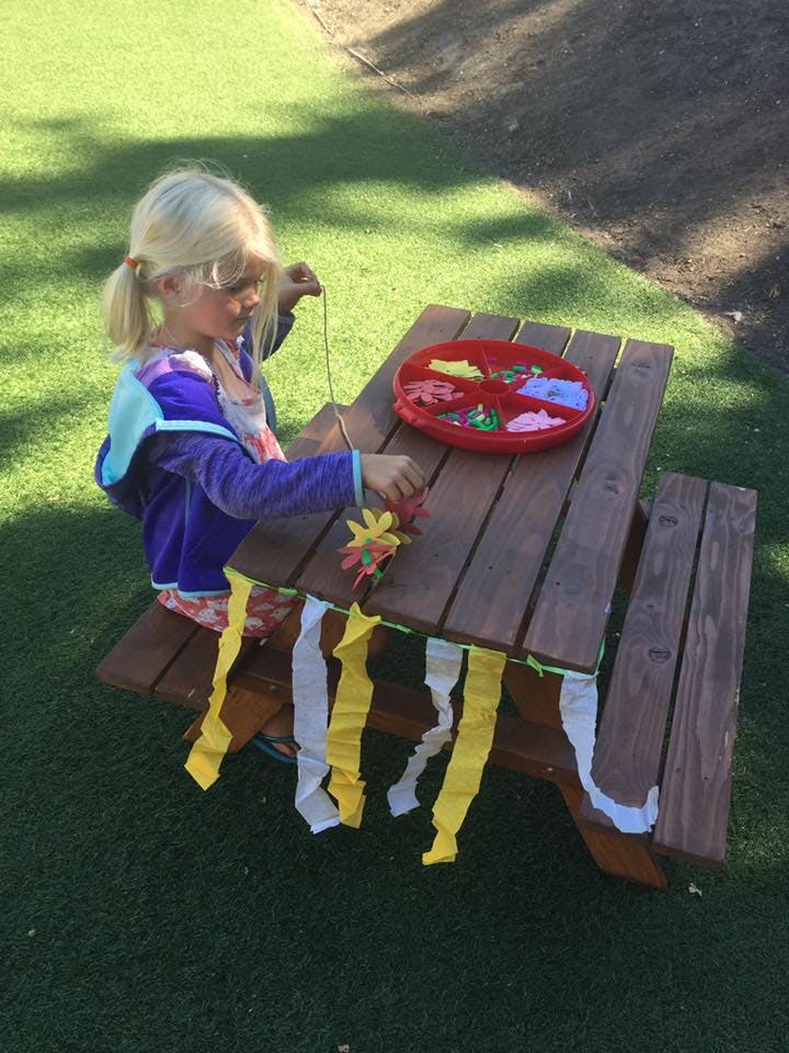 Child sitting at a picnic table stringing beads