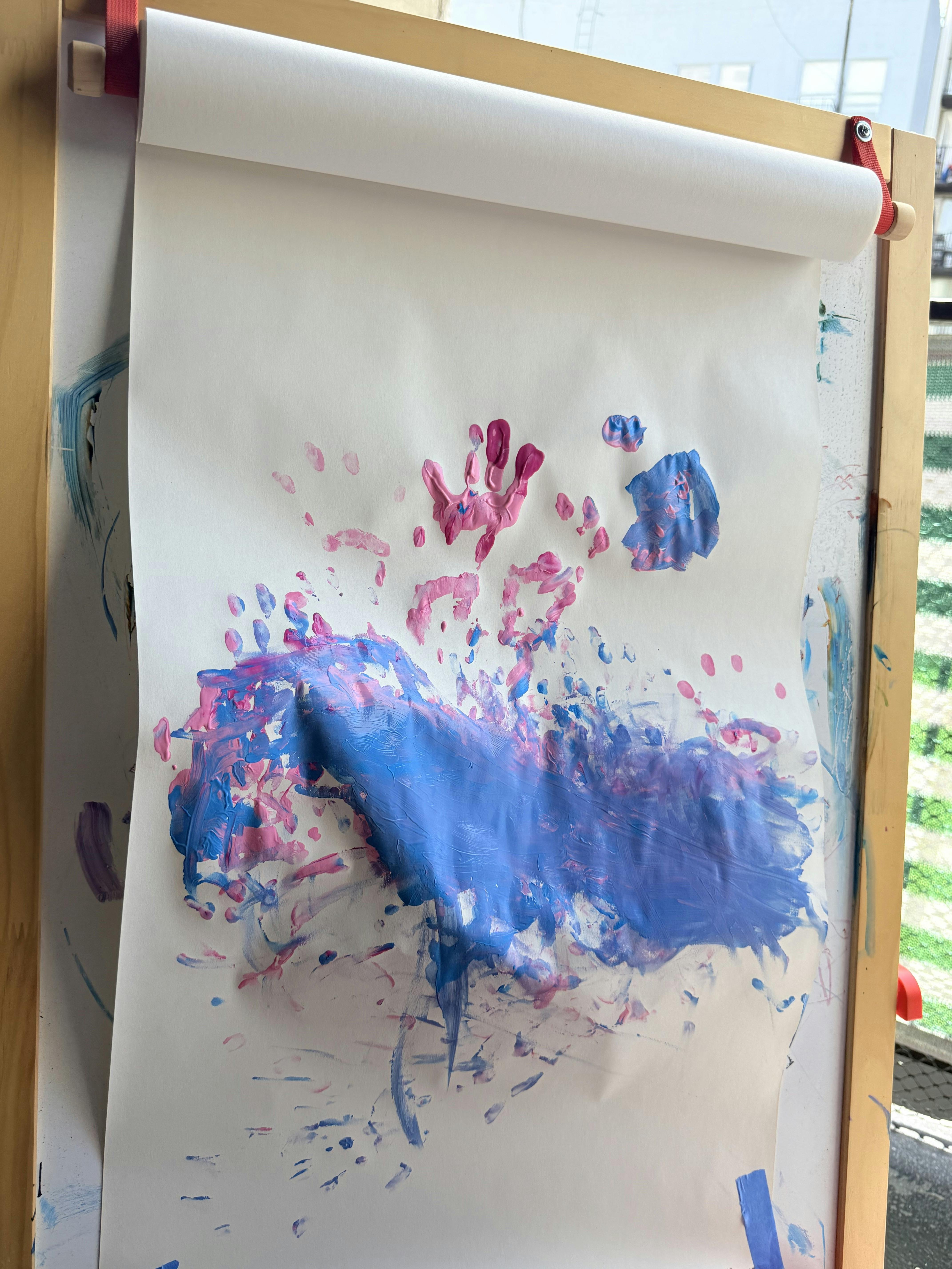 Child handprints and paint strokes on paper mounted on a wooden easel