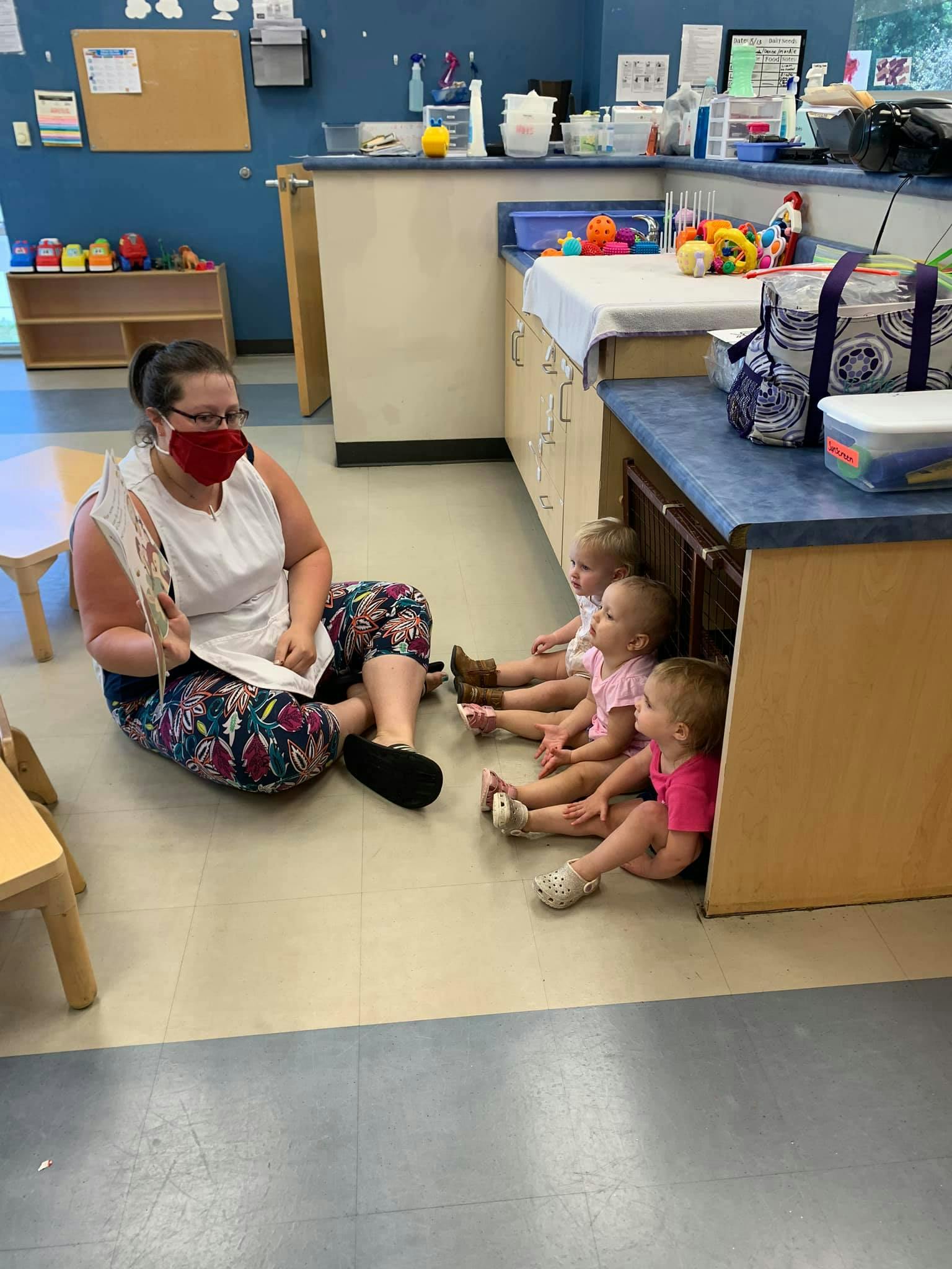 Person in mask reading to three children in a classroom