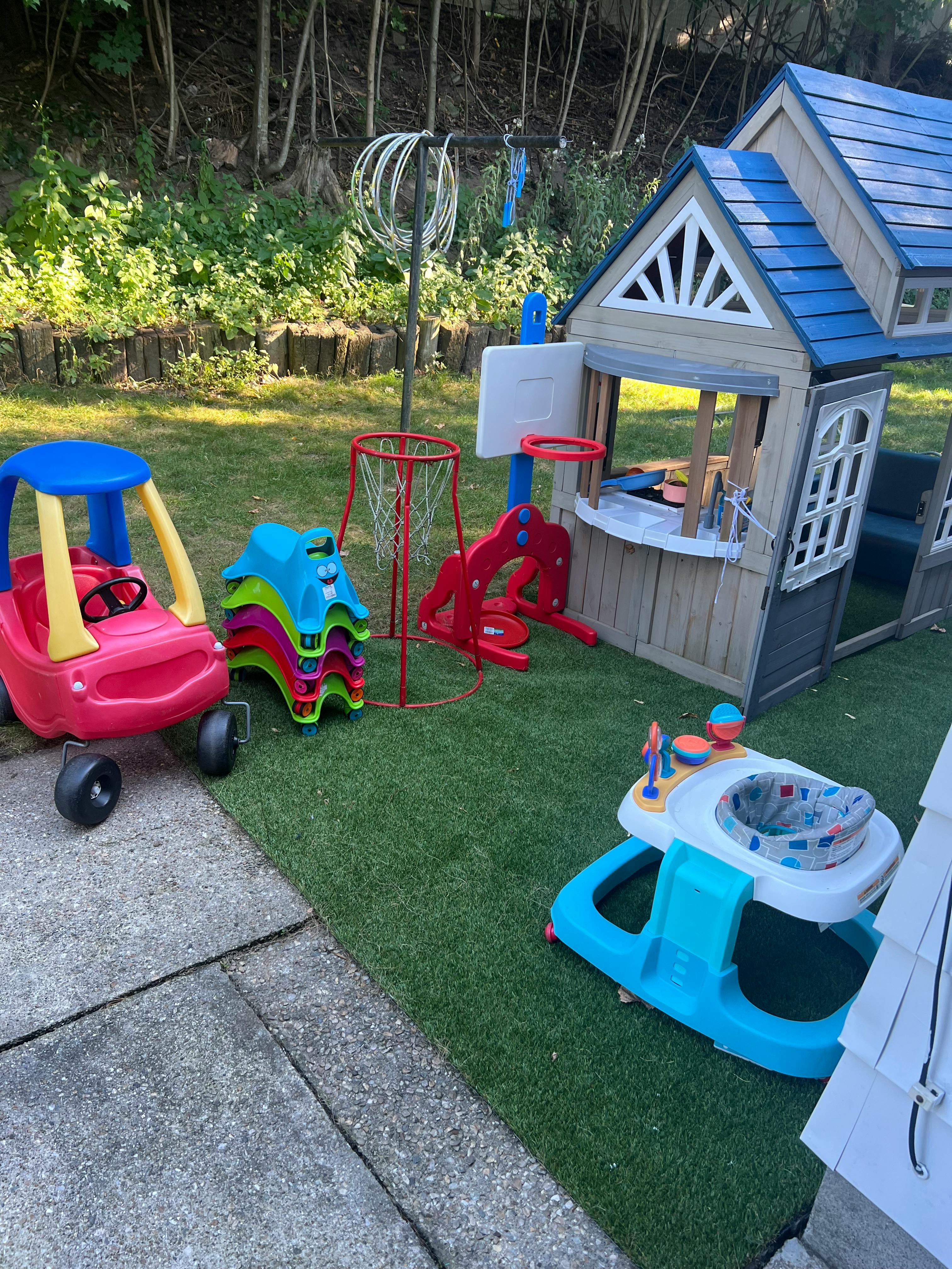 Children's playhouse, toy car, basketball hoop, and baby walker on grass