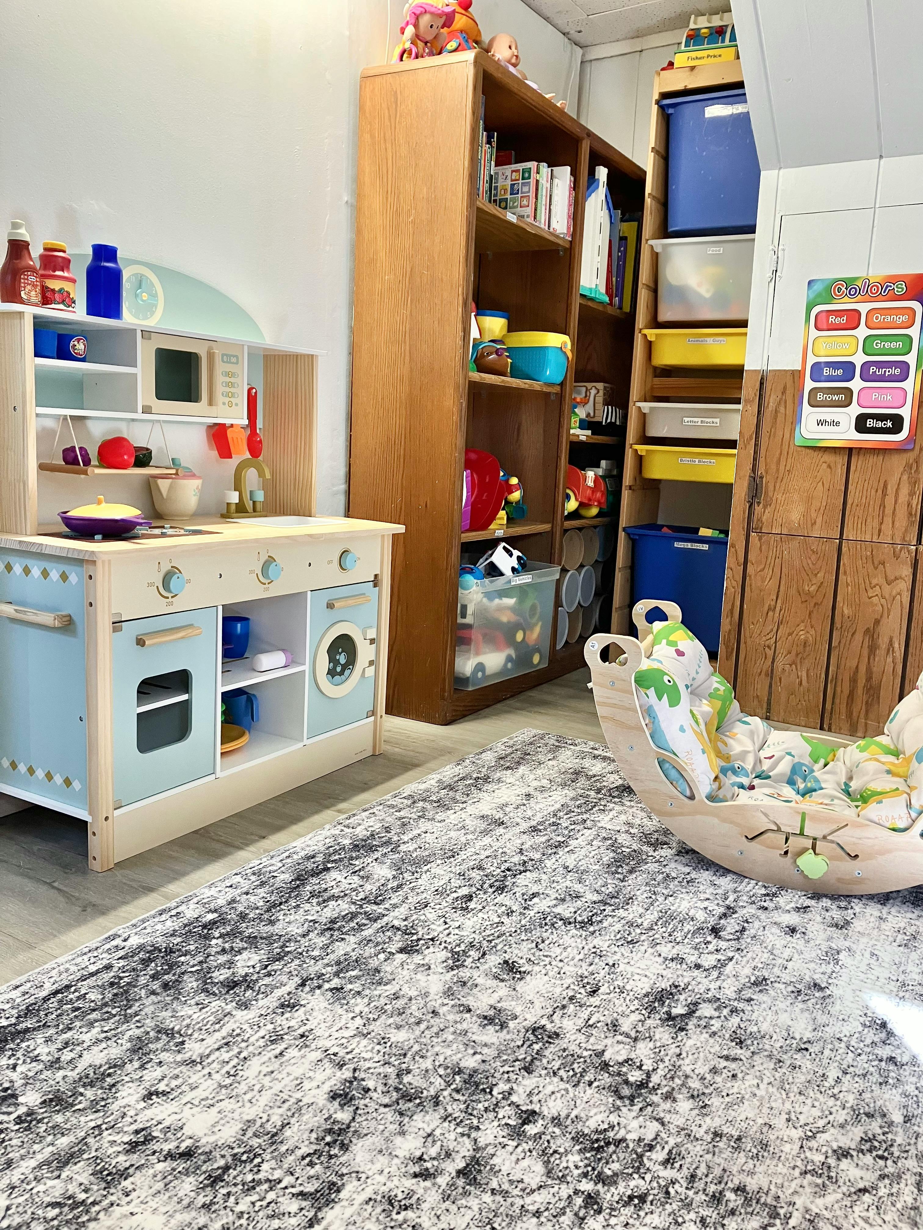 Play kitchen, wooden shelves with toys, and a wooden child's rocker in a room