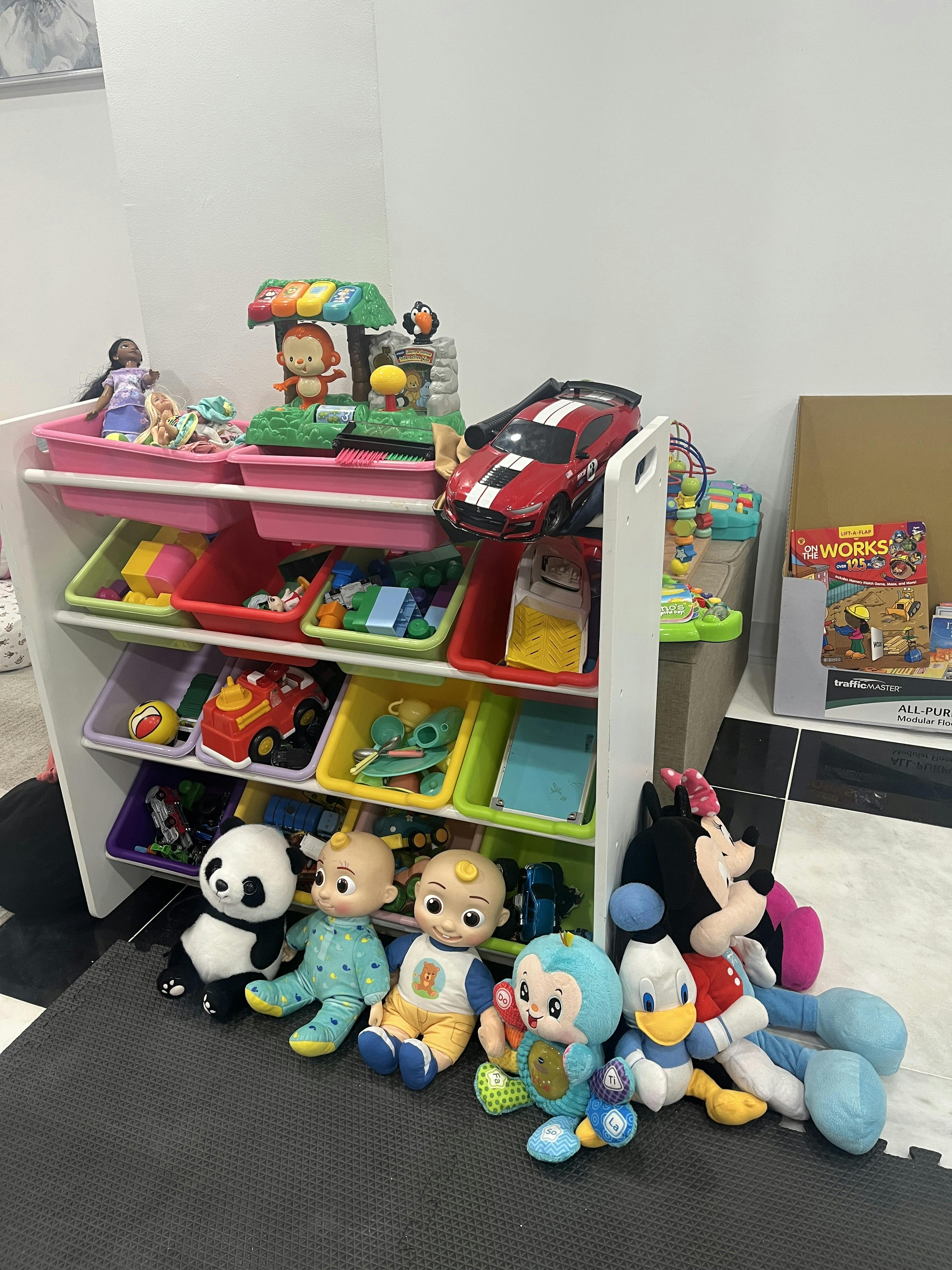 A toy storage organizer with plastic bins filled with various toys and plushies