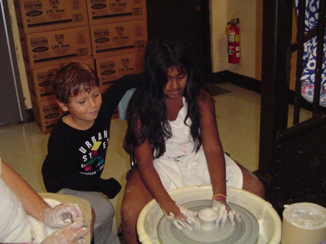 Teen and child making pottery on a wheel