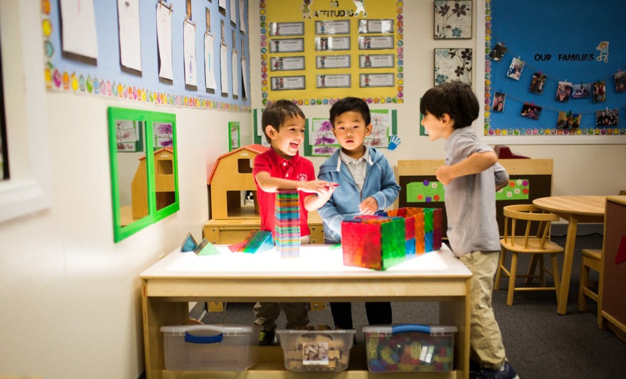 Three children playing with colorful blocks on a light table in a classroom