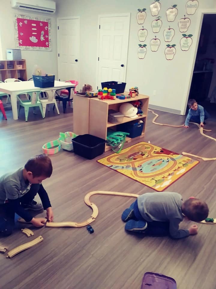 Three children playing with wooden train tracks on the floor of a room