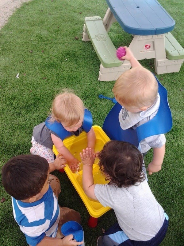 Children playing with a yellow water table on grass