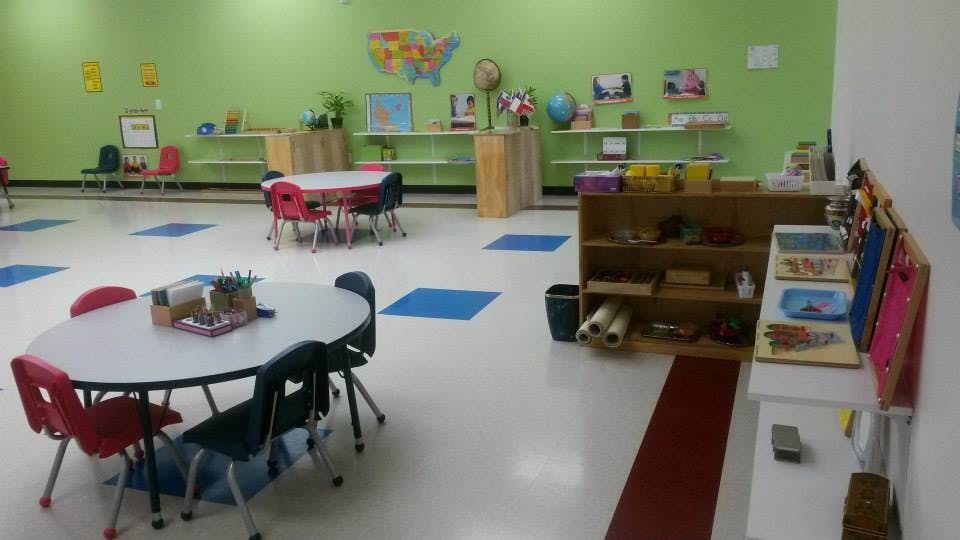 Classroom with small tables and chairs, shelves with learning materials