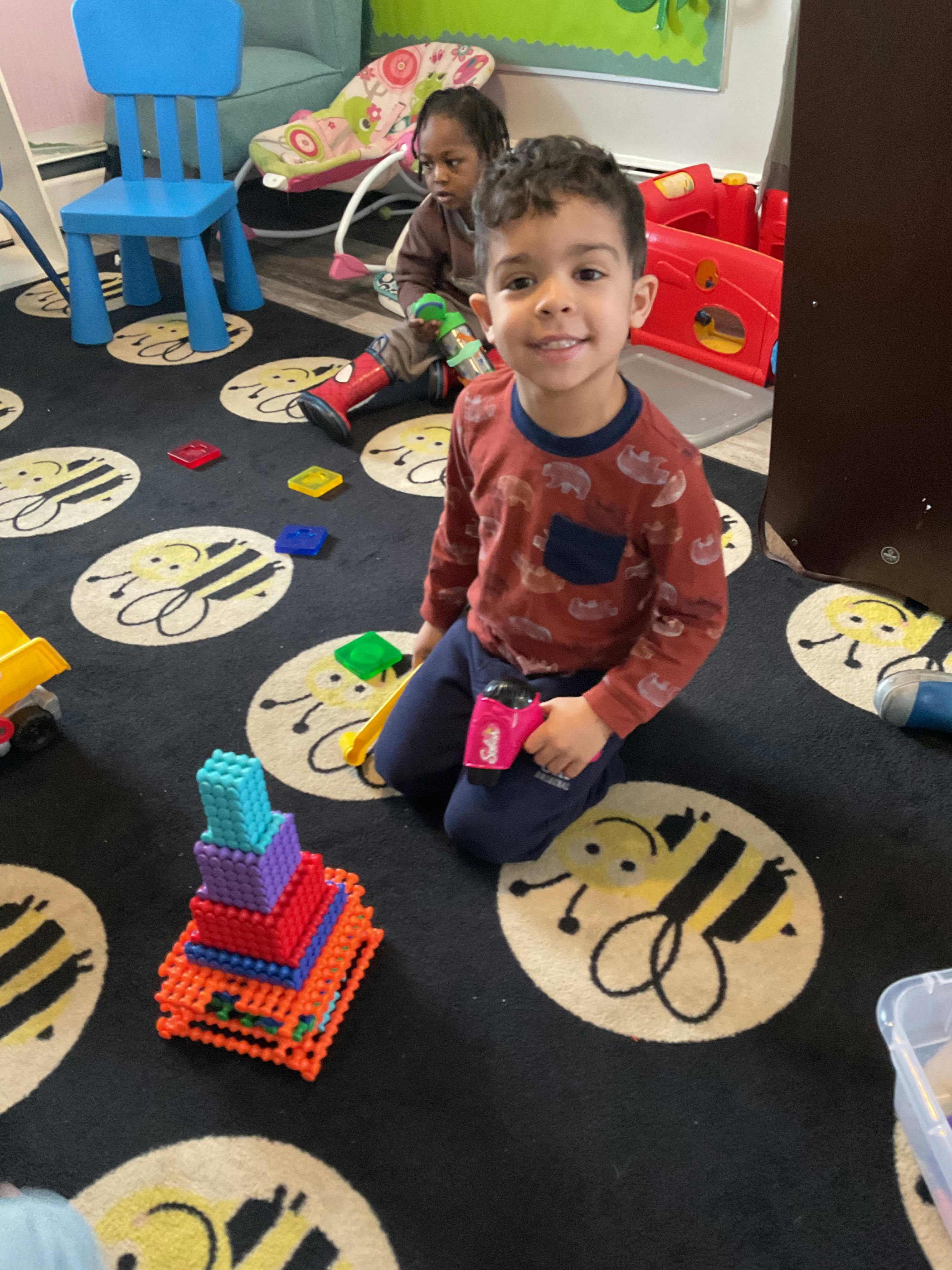 Children playing with building blocks on a rug with bee patterns