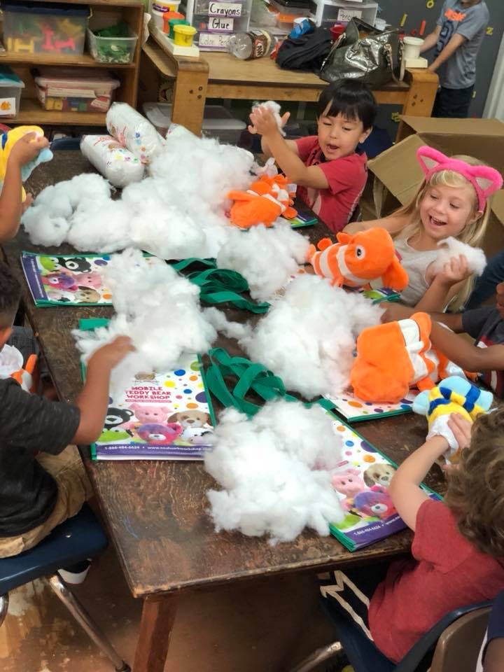 Children stuffing plush toys with white filling at a table