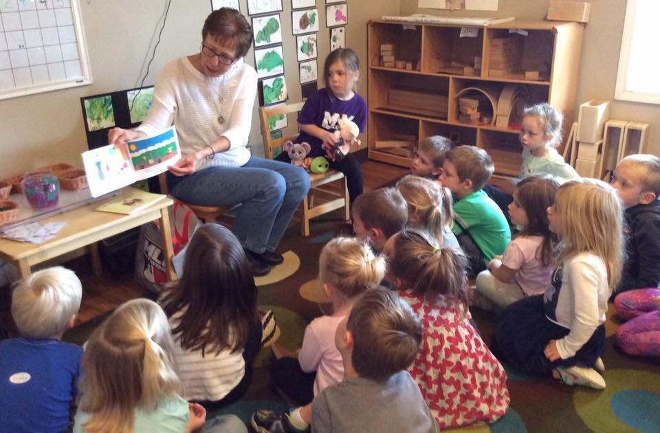 Adult reading a book to a group of children in a classroom