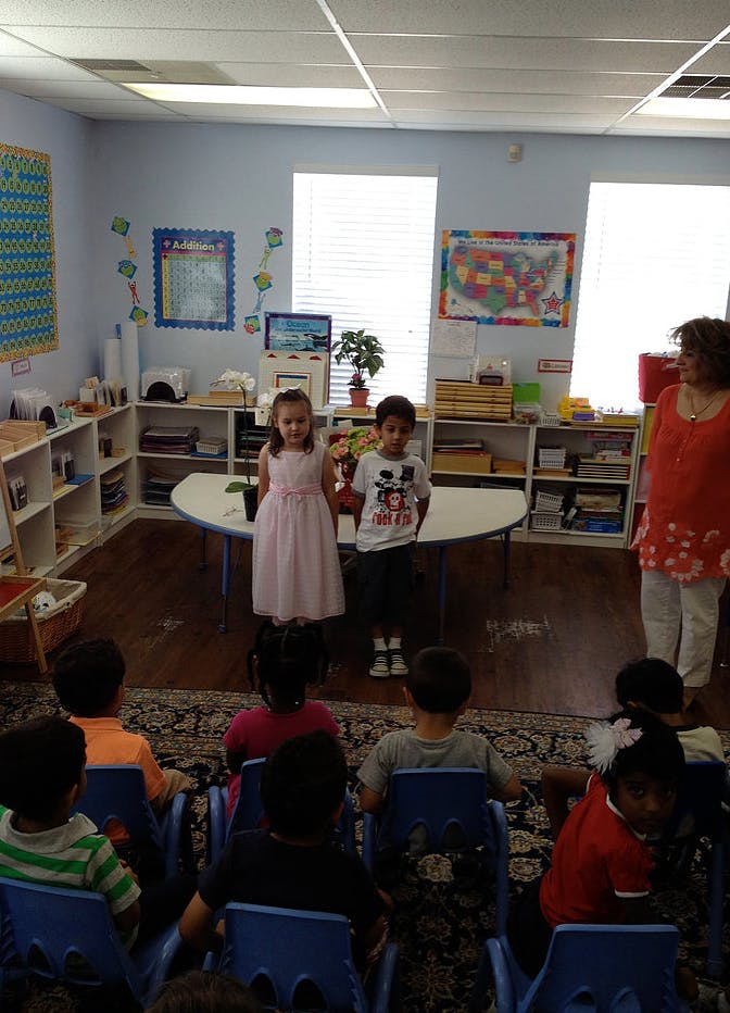 Two children standing in front of seated children in a classroom