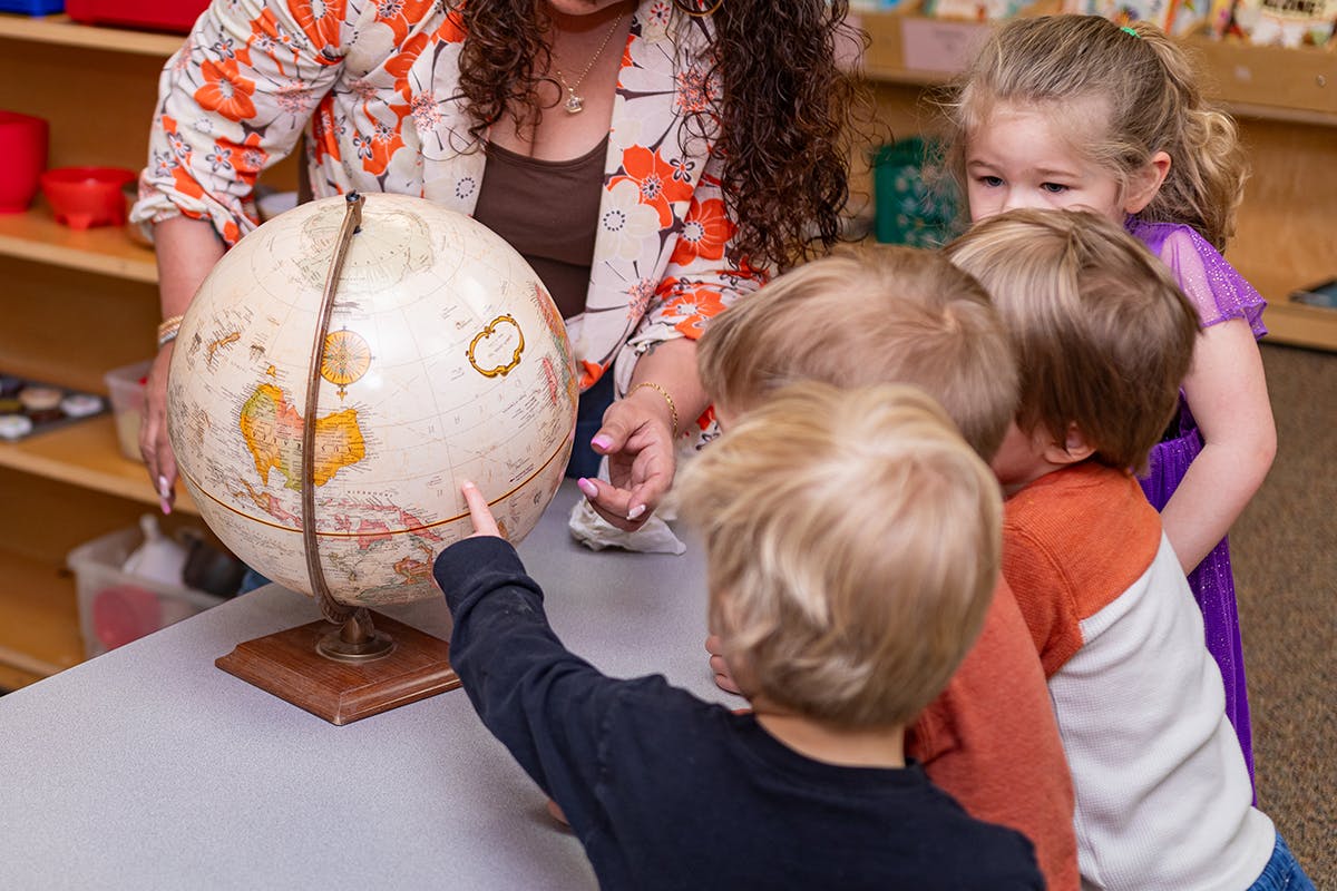 Person and children looking at a globe in a classroom