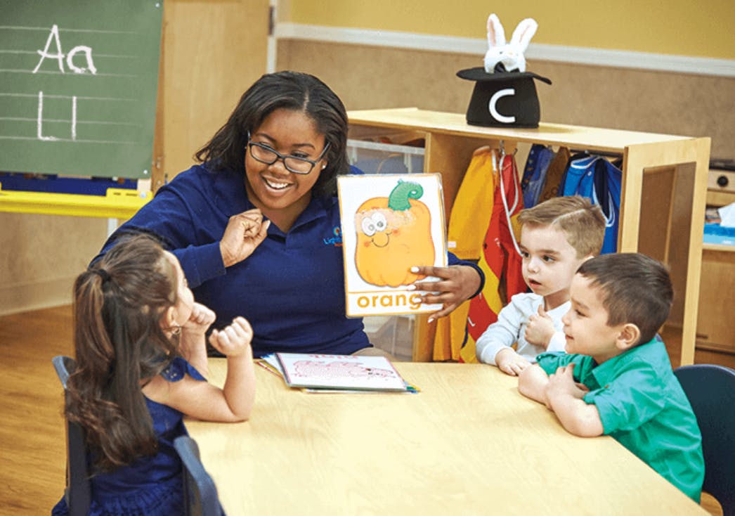 Person showing a picture of an orange to three children in a classroom