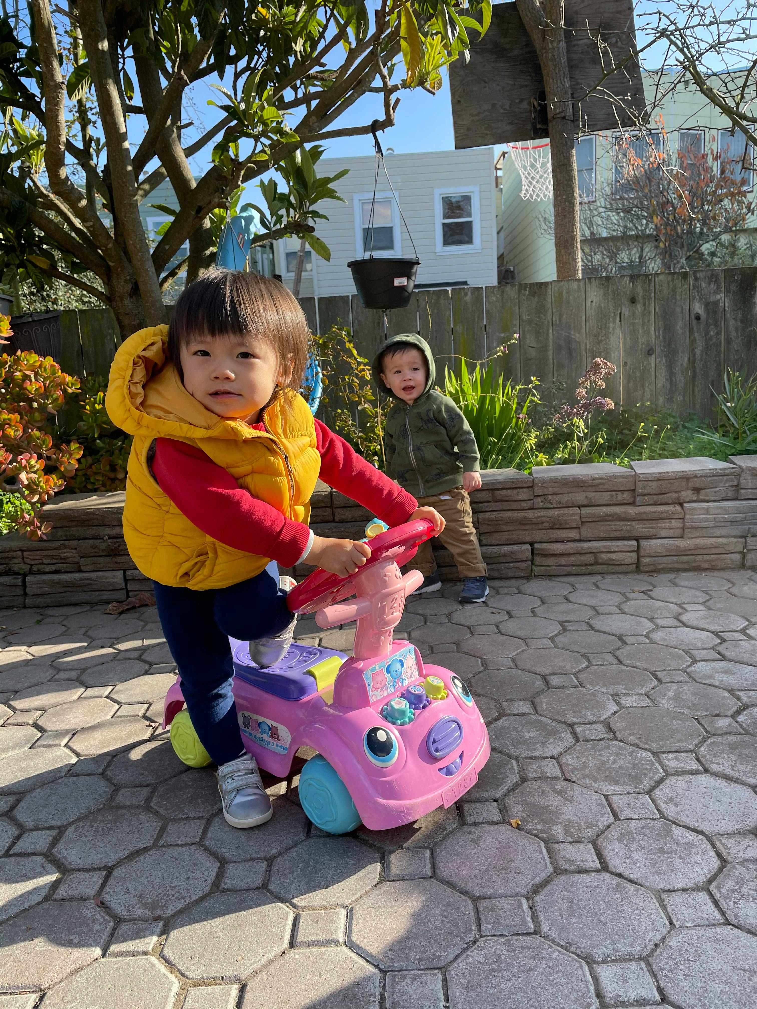 Child on a pink ride-on toy, another child in background