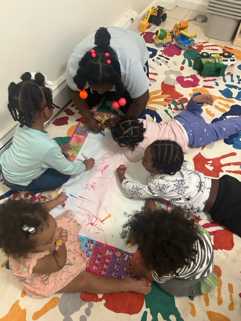 Adult and multiple children drawing on a large sheet of paper on the floor