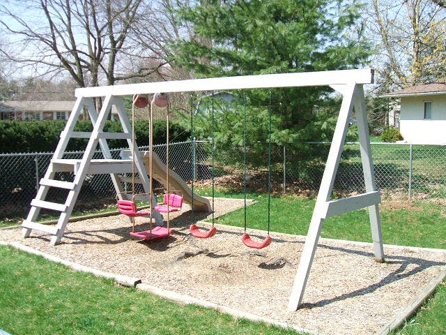 Swing set with a slide and multiple swings in a playground area with wood chips on the ground