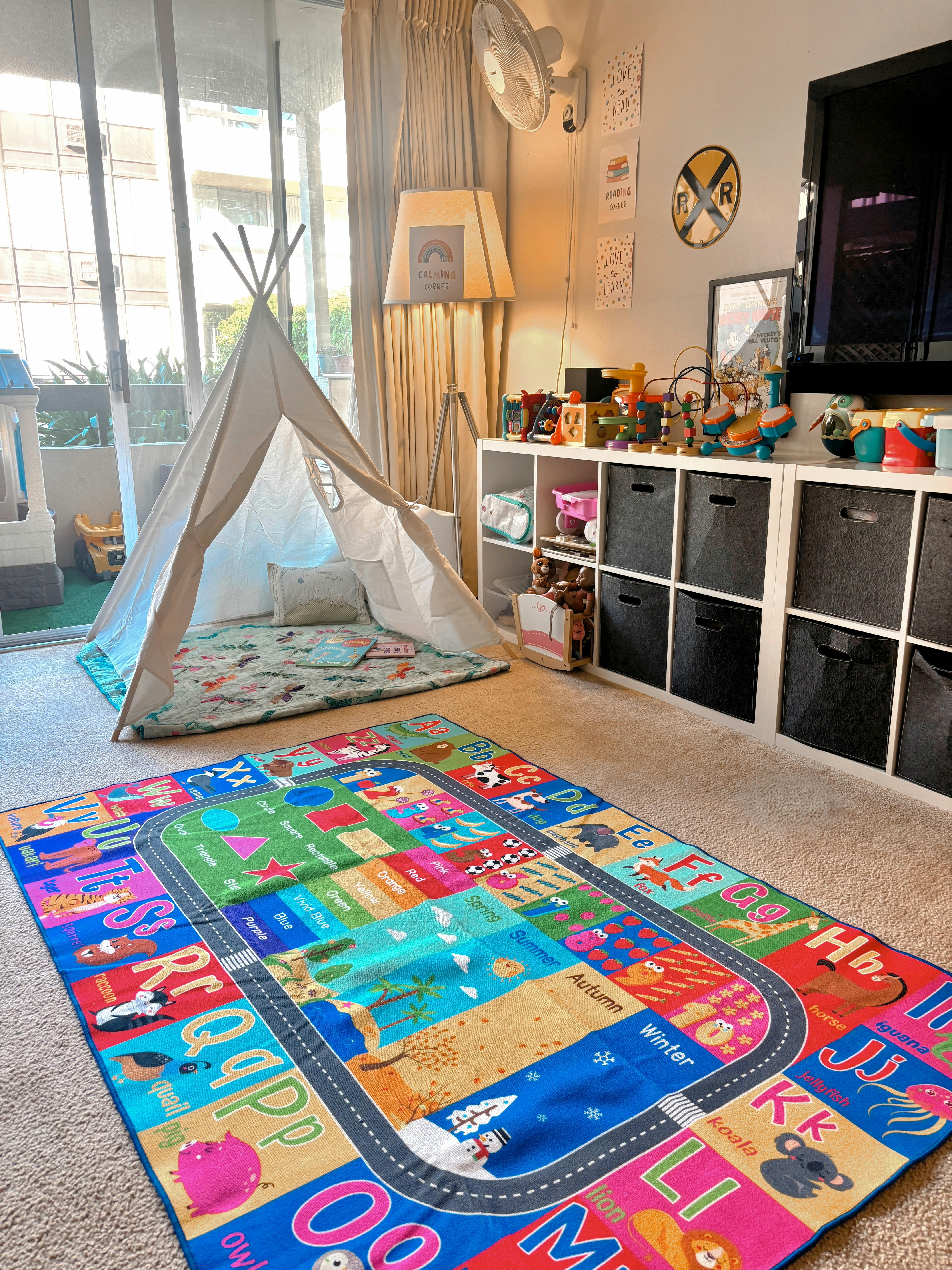 Child's play area with a teepee, alphabet rug, and toy shelves