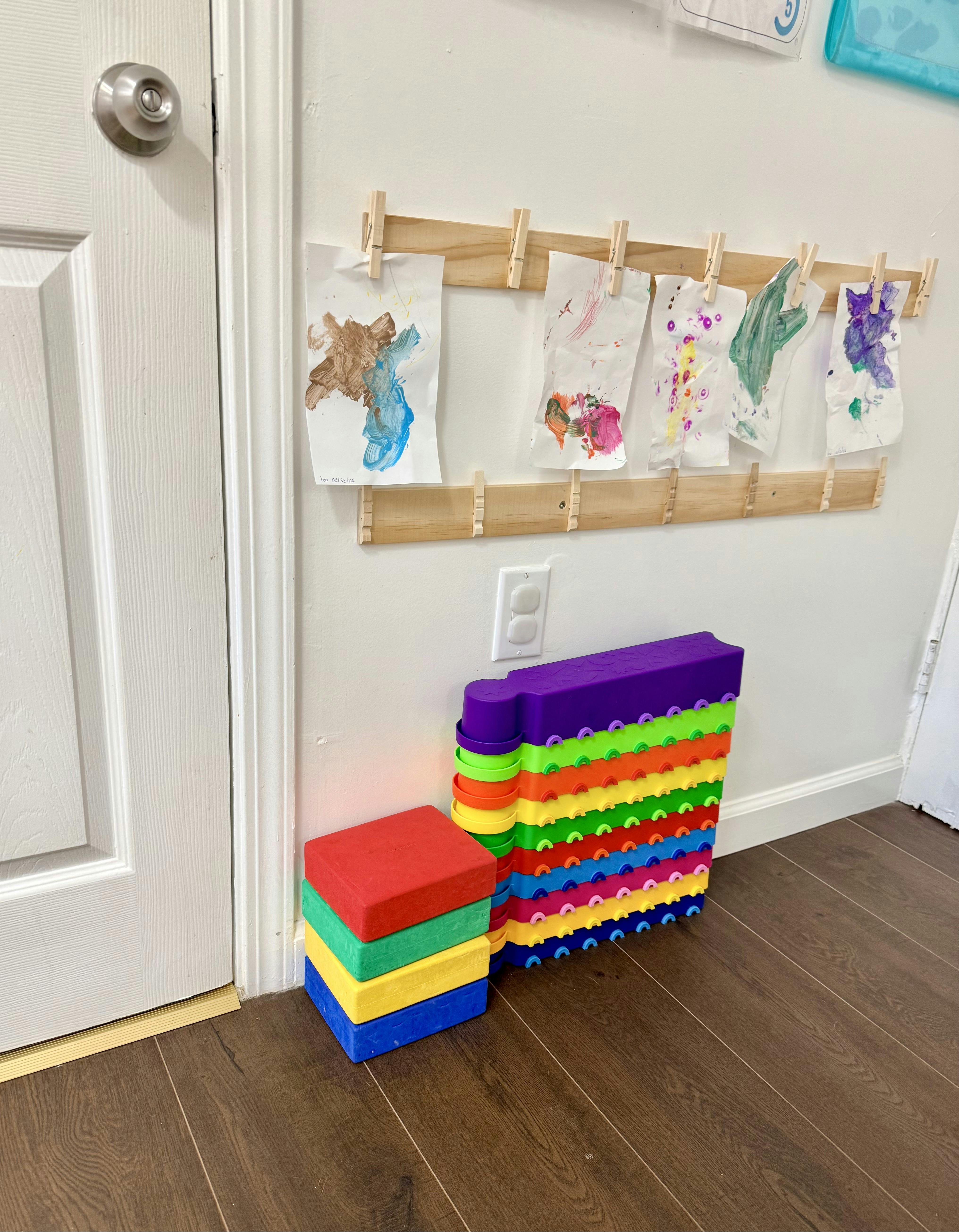 Child artwork hanging on wall clips above colorful toy blocks on the floor