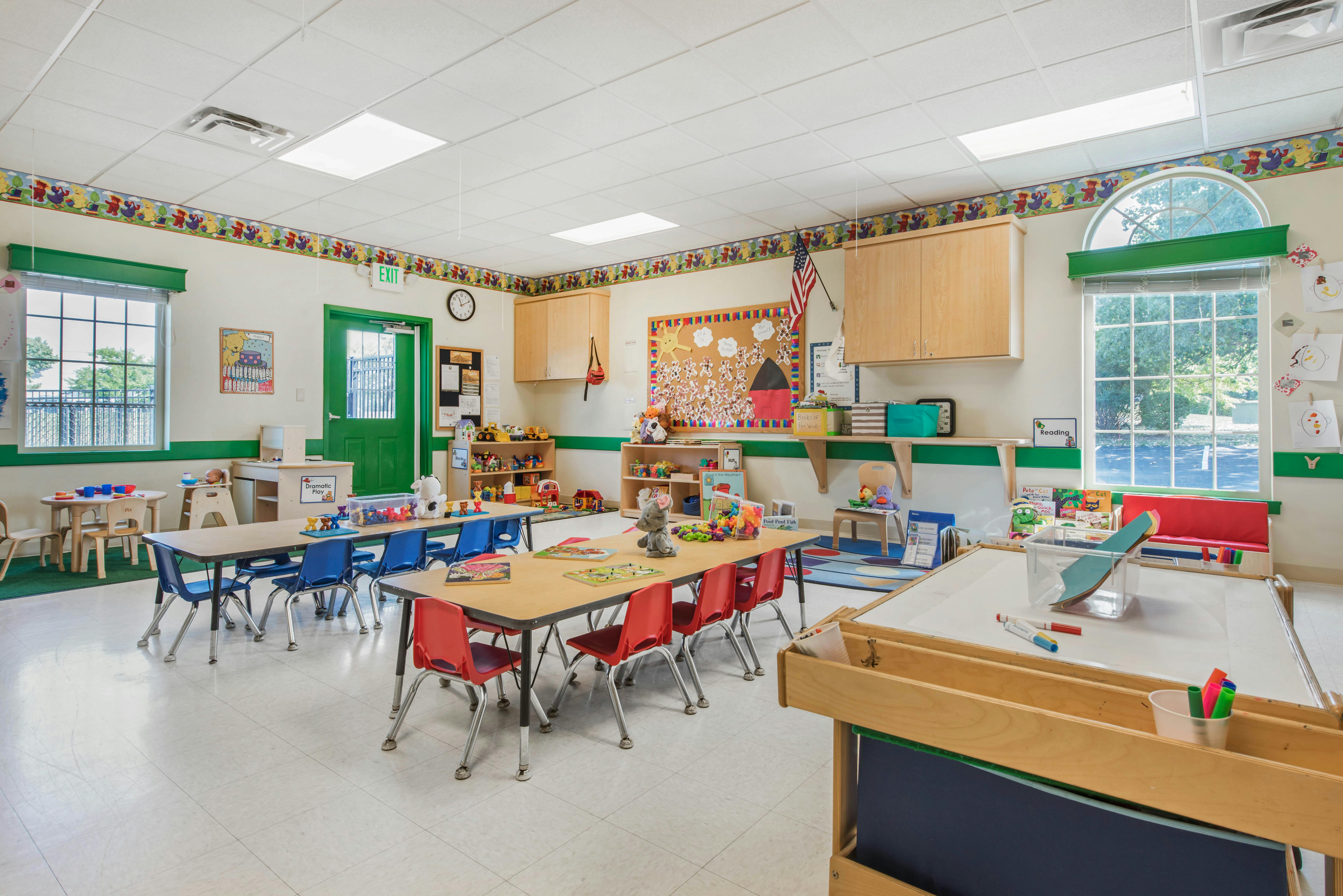 An empty preschool classroom with colorful tables, chairs, and learning materials
