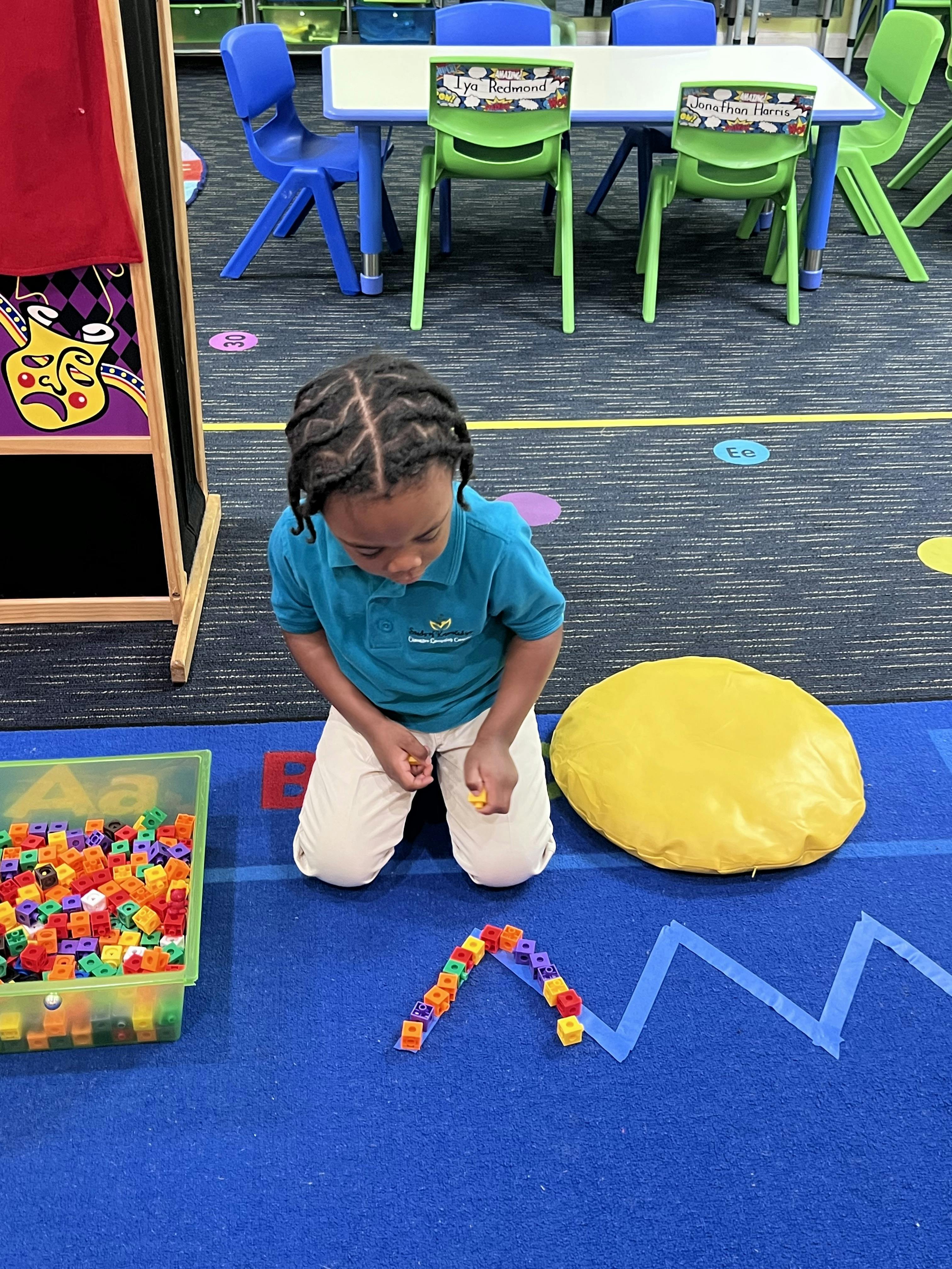 Child kneeling on a blue rug, playing with colorful connecting cubes