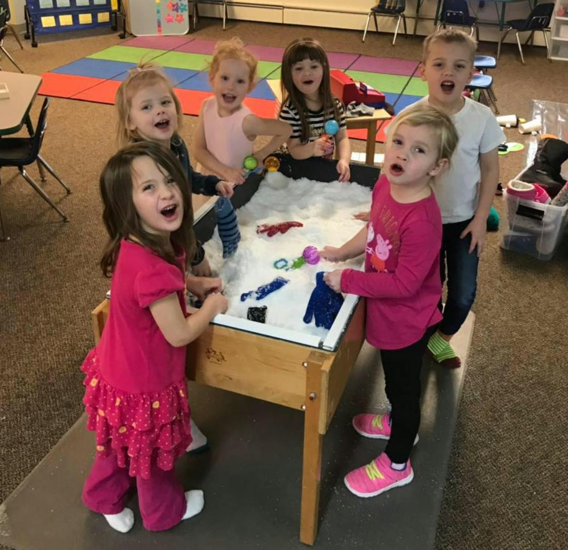 Children playing at a sand table in a classroom