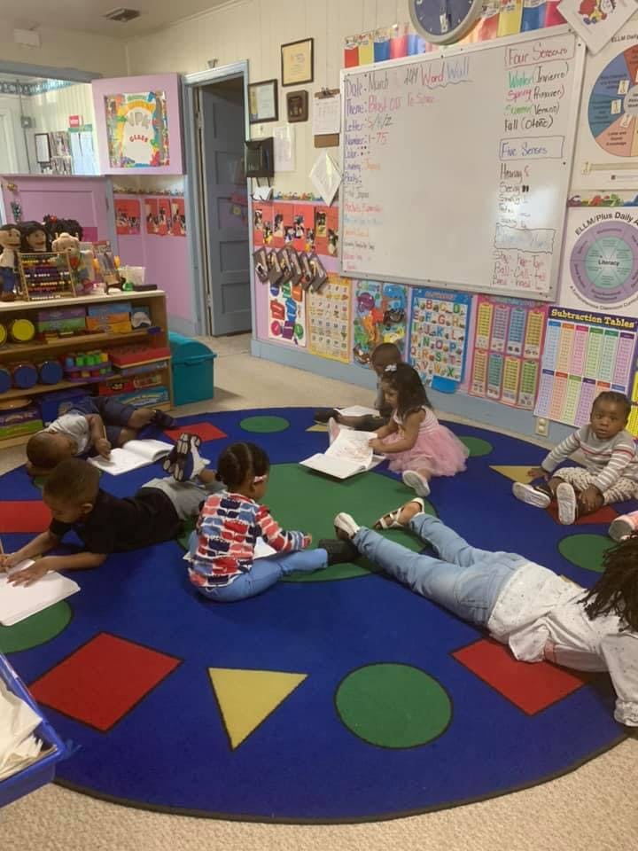 Children sitting and lying on a rug in a classroom, looking at papers