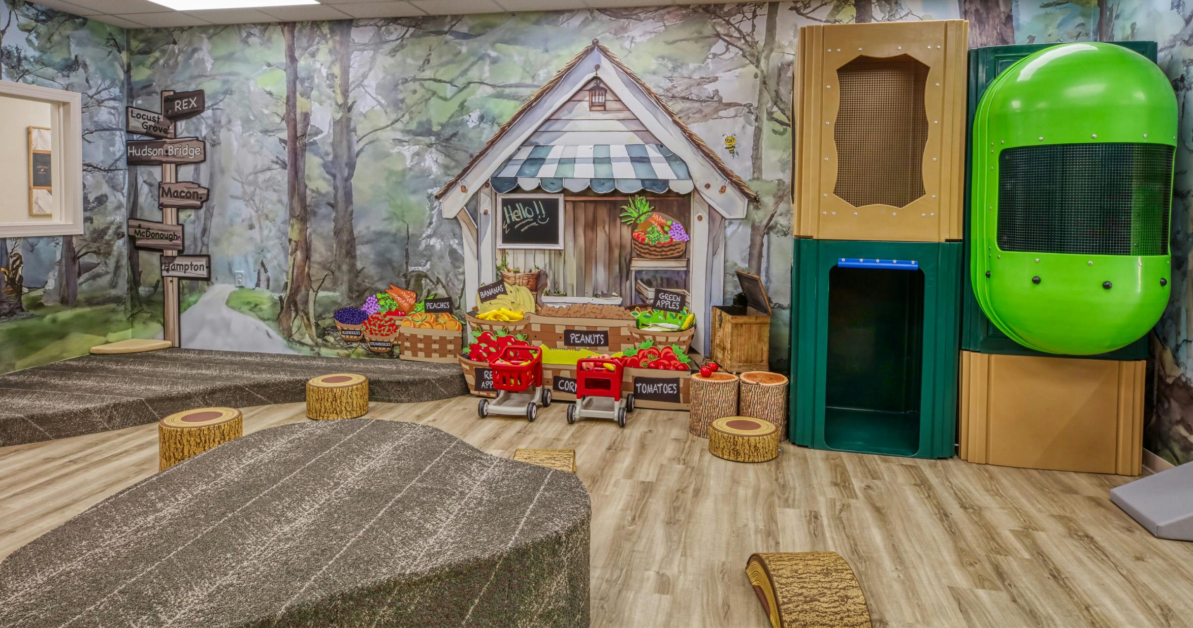 Indoor play area with a market stall, woodland mural, and playground equipment