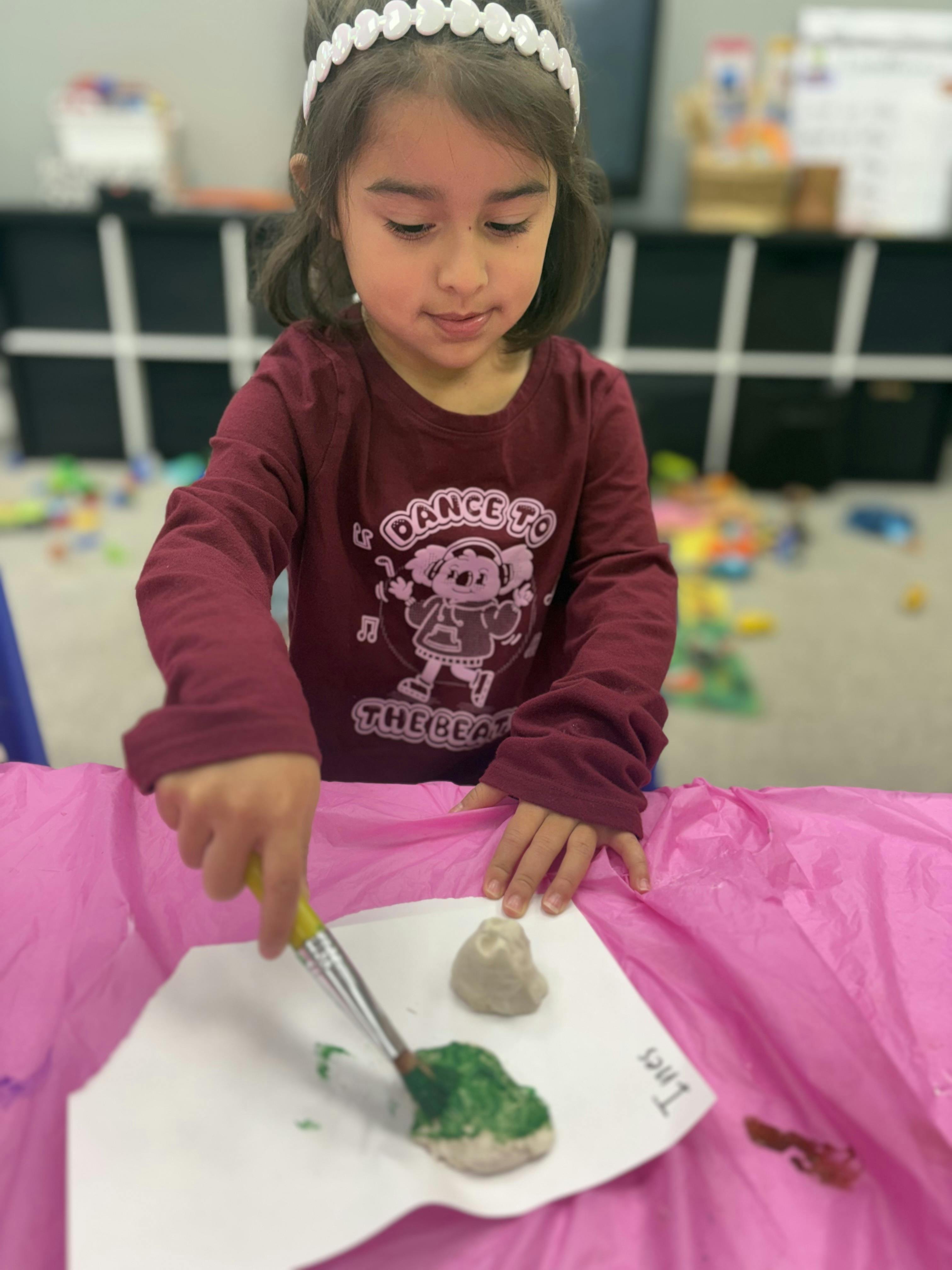 Child painting a rock green with a paintbrush