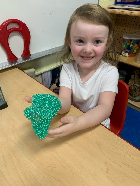 Child holding green foam clay at a table