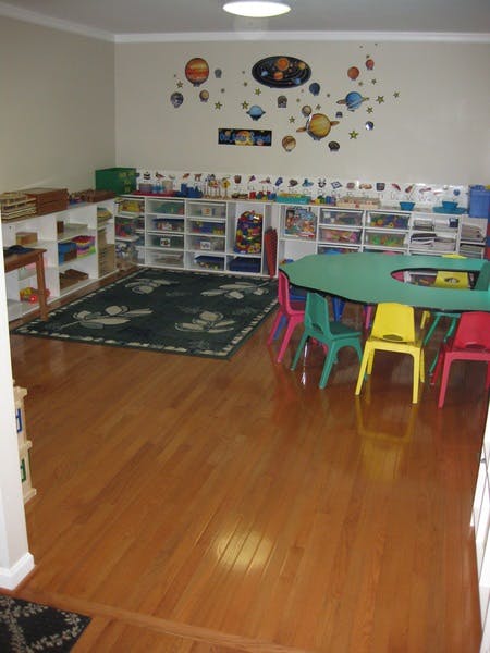 Classroom with shelves of toys, a rug, and a green table with colorful chairs