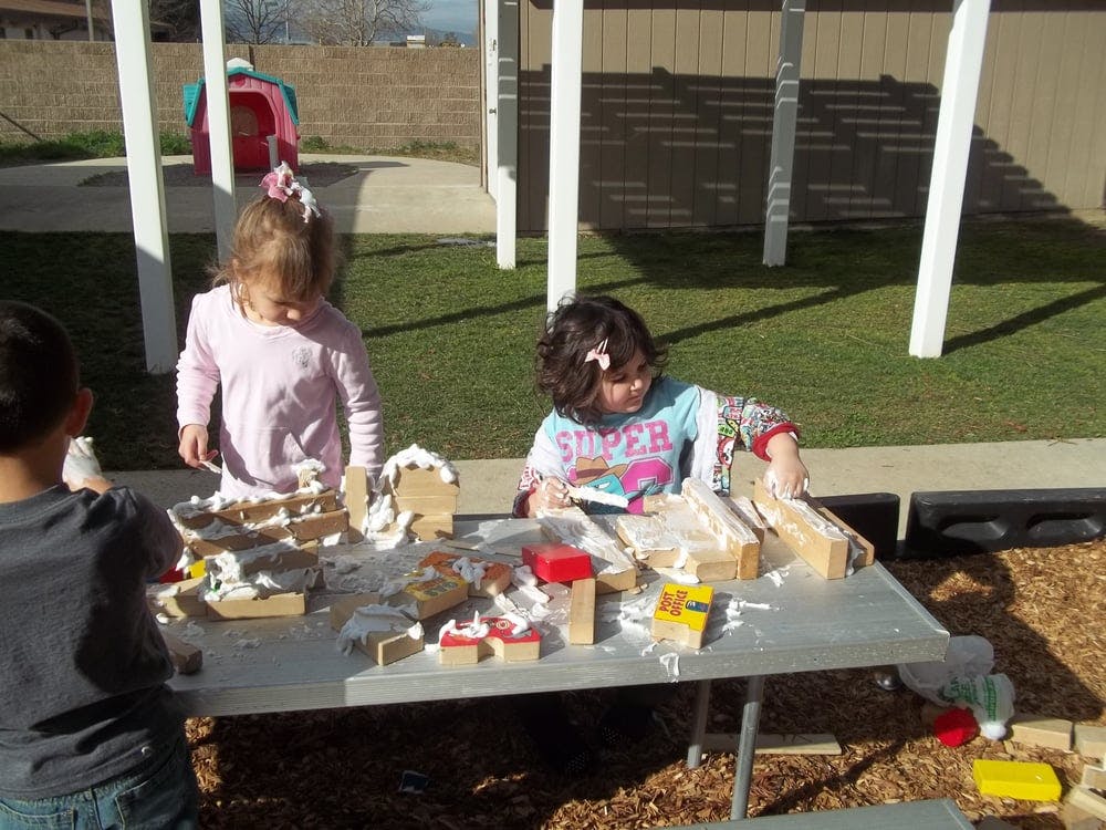 Three children playing with blocks and white foam at a table outdoors