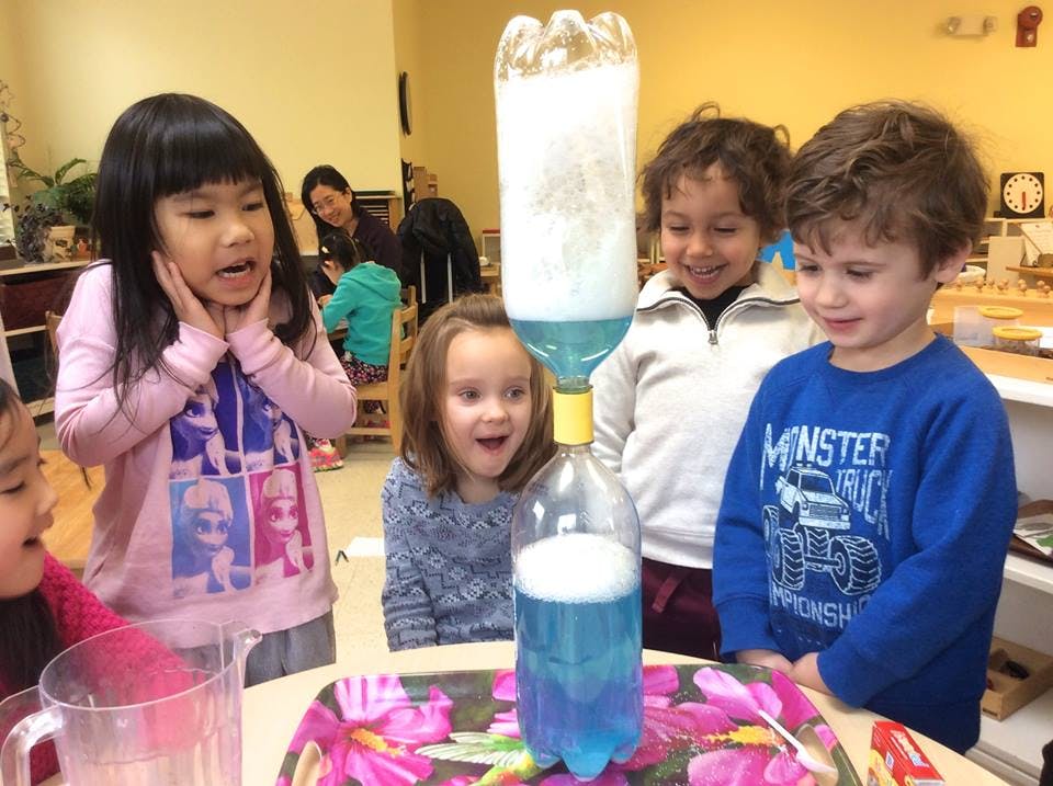 Children watching a science experiment with bottles and two plastic bottles