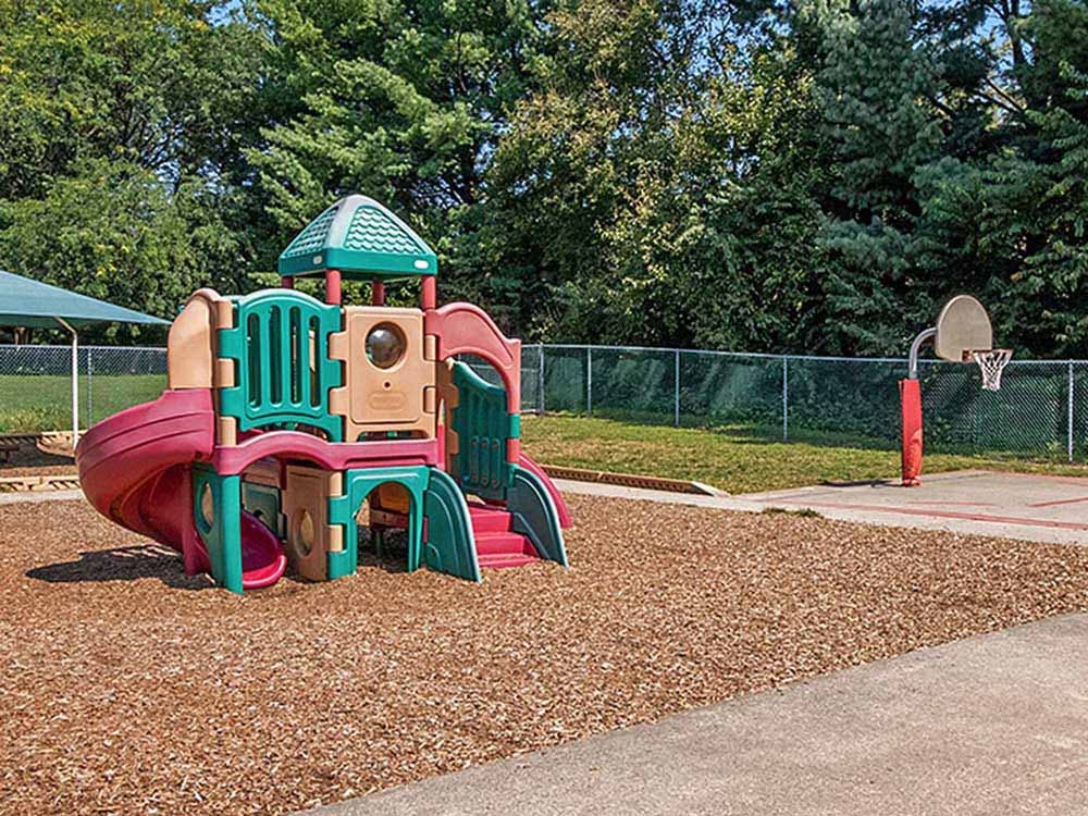 Playground equipment and a basketball hoop on wood chips and concrete