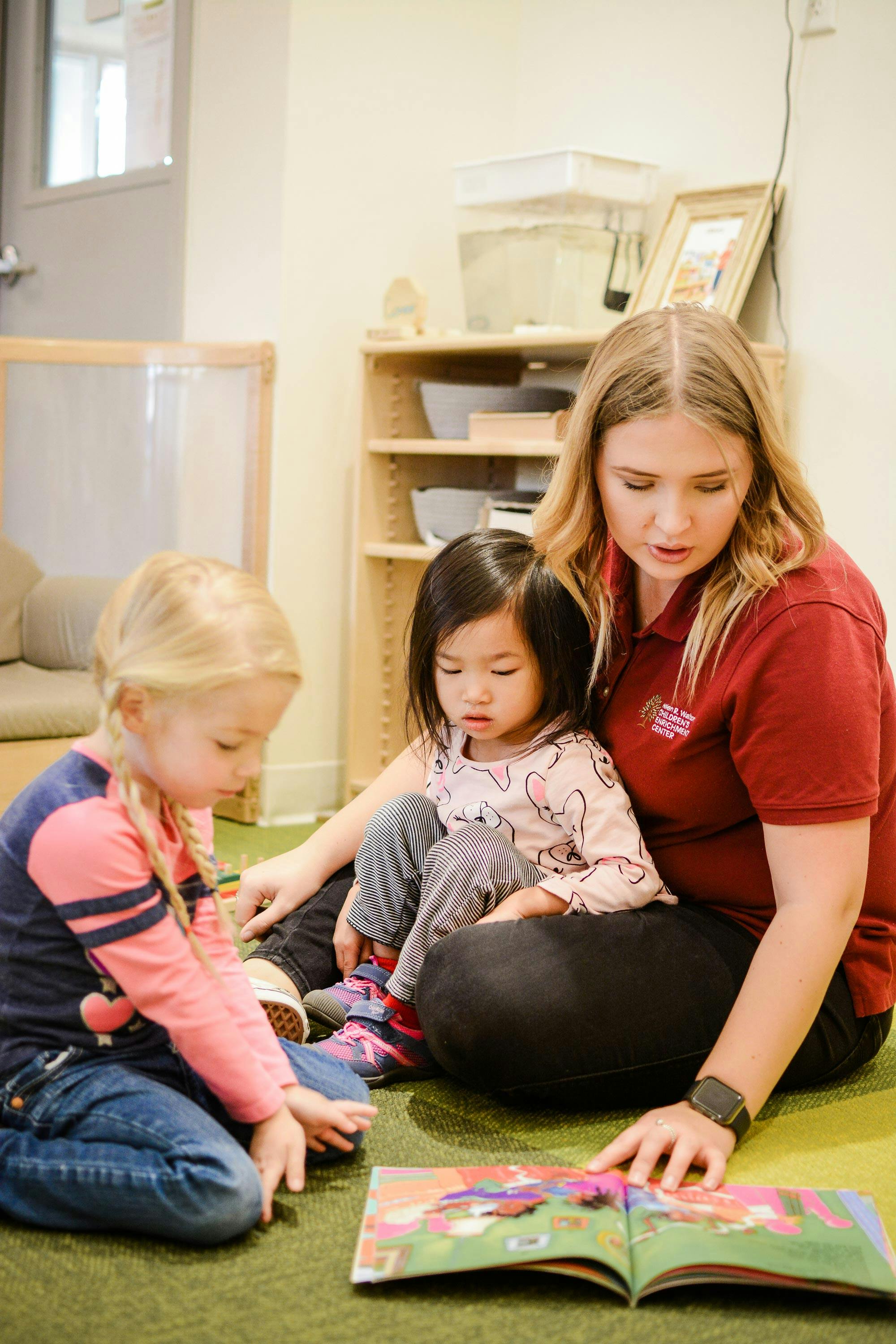 Person reading a book to two children in a classroom