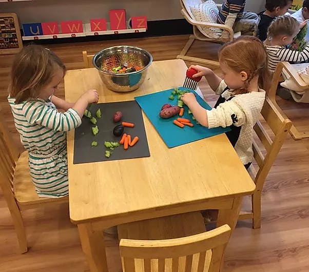 Two children at a table cutting vegetables