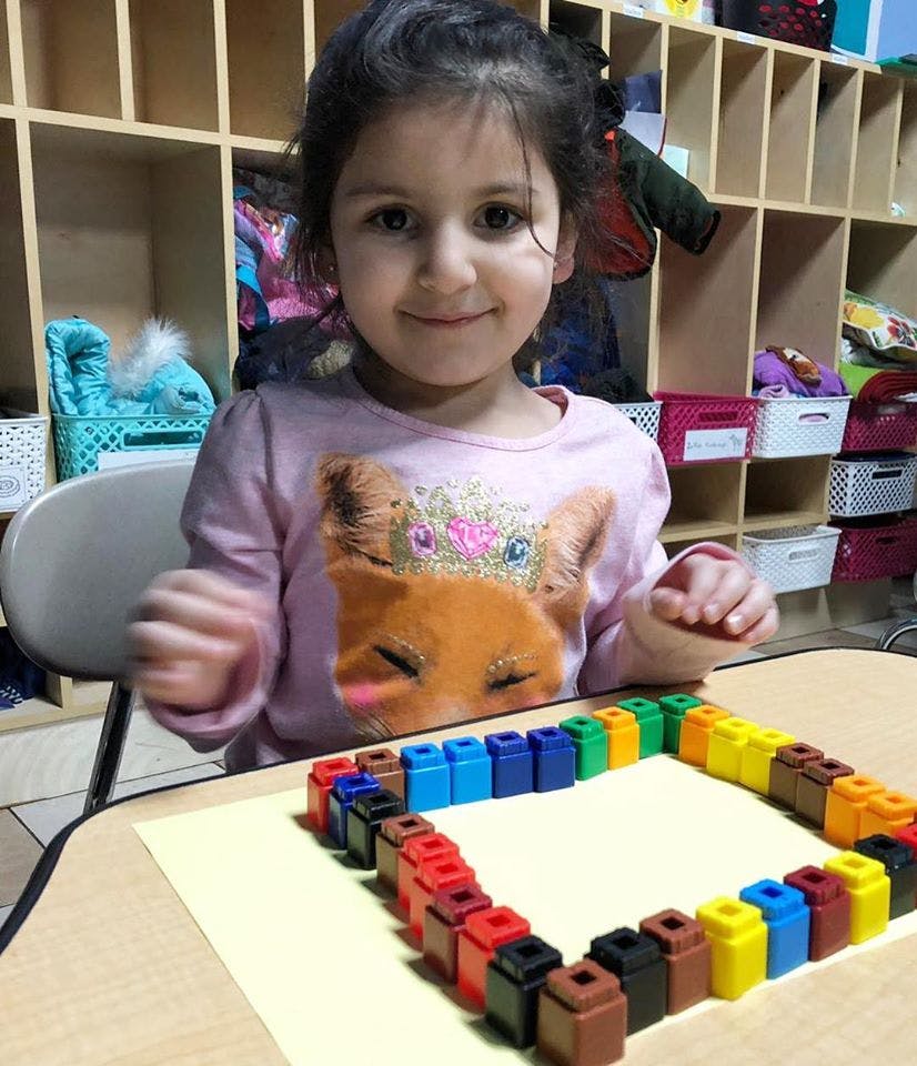 Child at a table with colorful connecting blocks arranged in a square