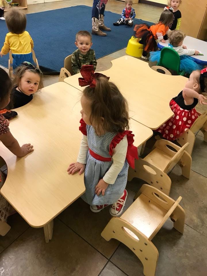 Children standing and sitting around small tables in a classroom