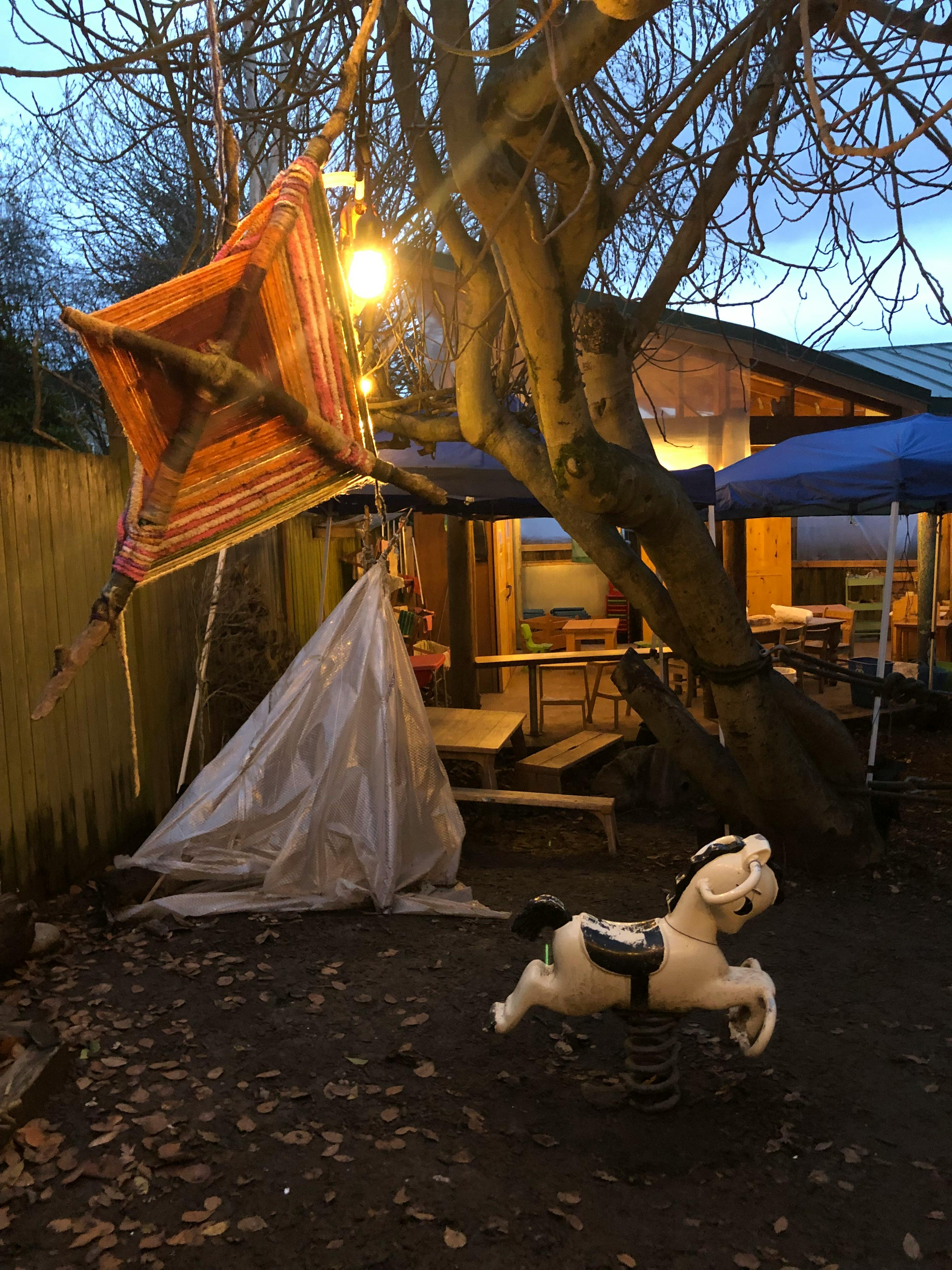 Rocking horse in a yard with a tree and a structure in the background