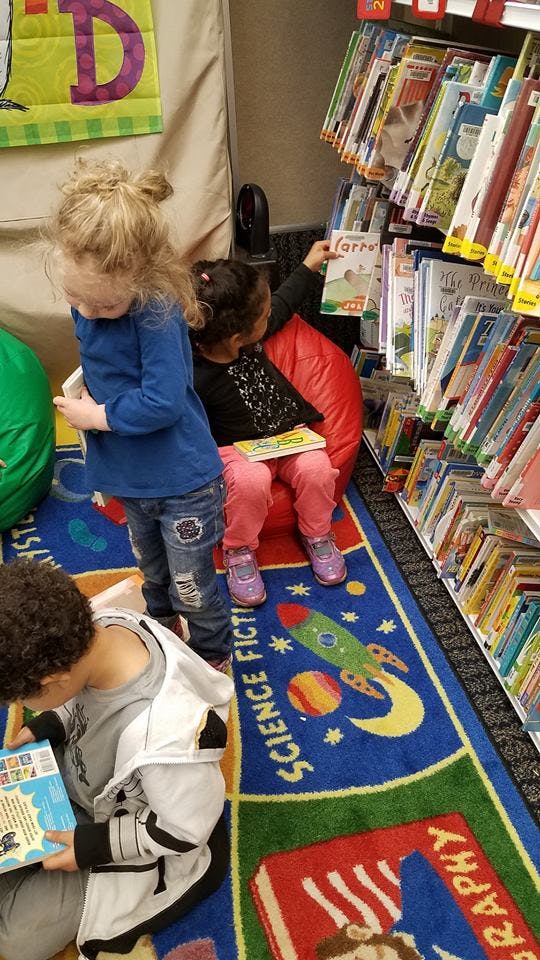 Three children reading books in a library