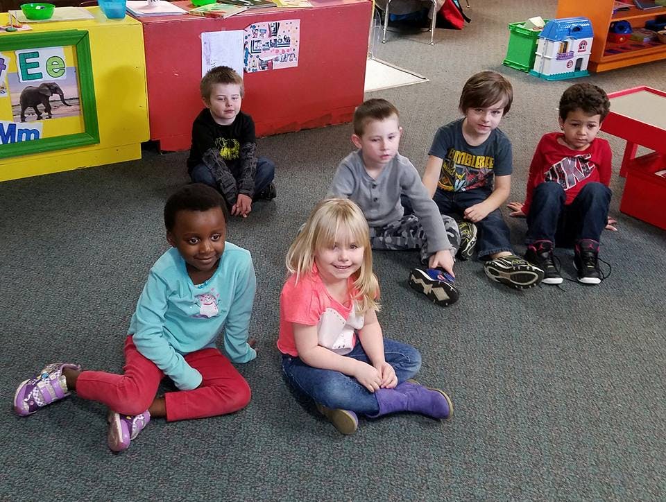 Five children sitting on a carpeted floor in a classroom