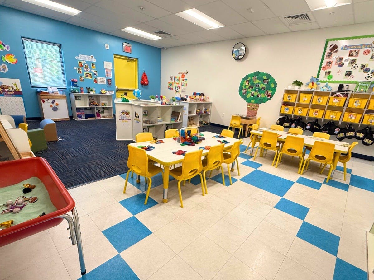 Classroom with small tables and chairs, shelves with toys, and blue and white floor tiles