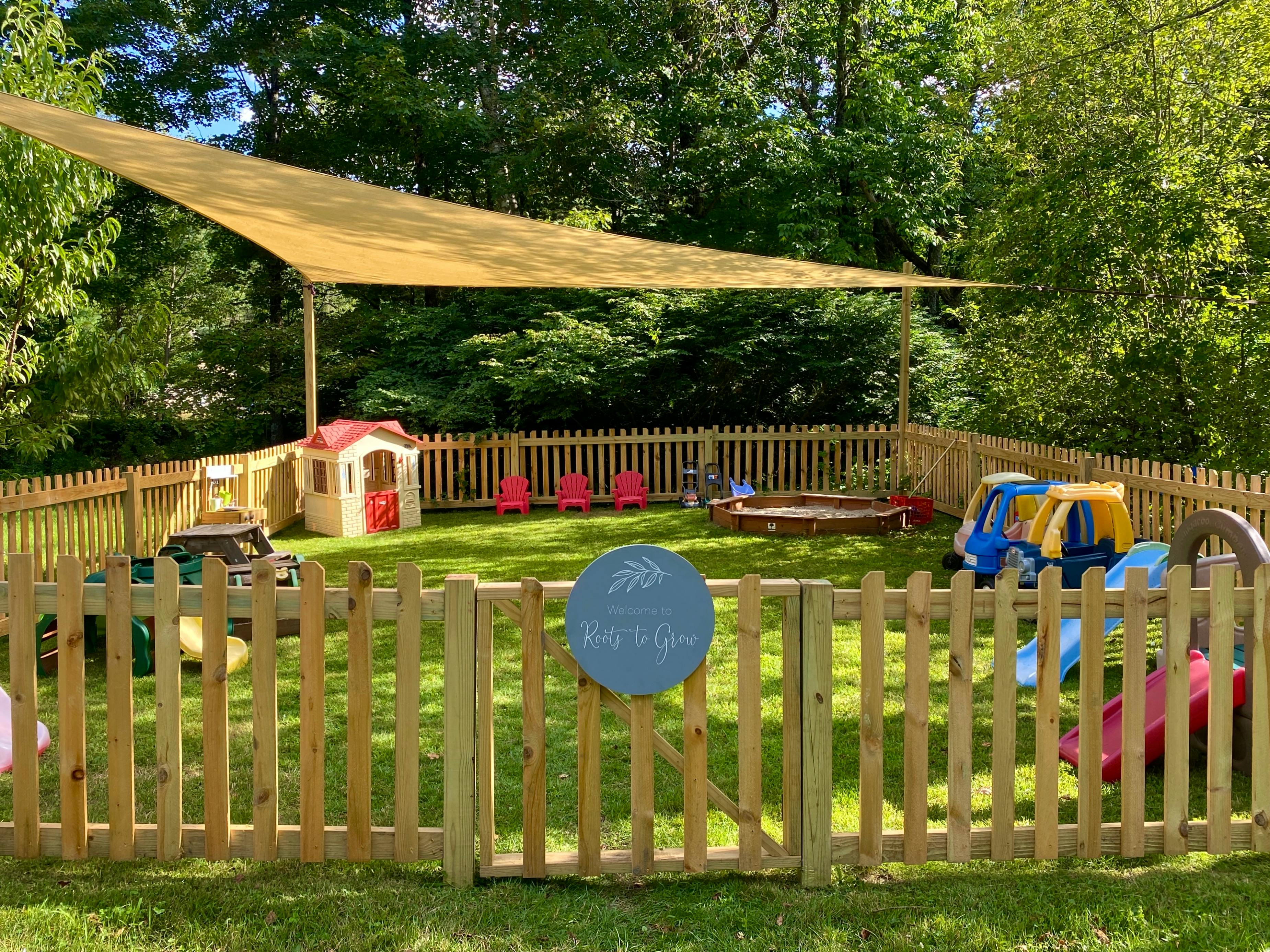 A fenced-in outdoor play area with various toys under a shade sail
