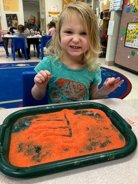 Child sitting at a table with a tray of orange sand