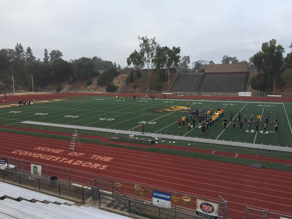 Marching band practicing on a football field with stadium seating