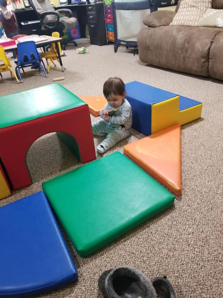 Child sitting on carpet surrounded by colorful soft play blocks