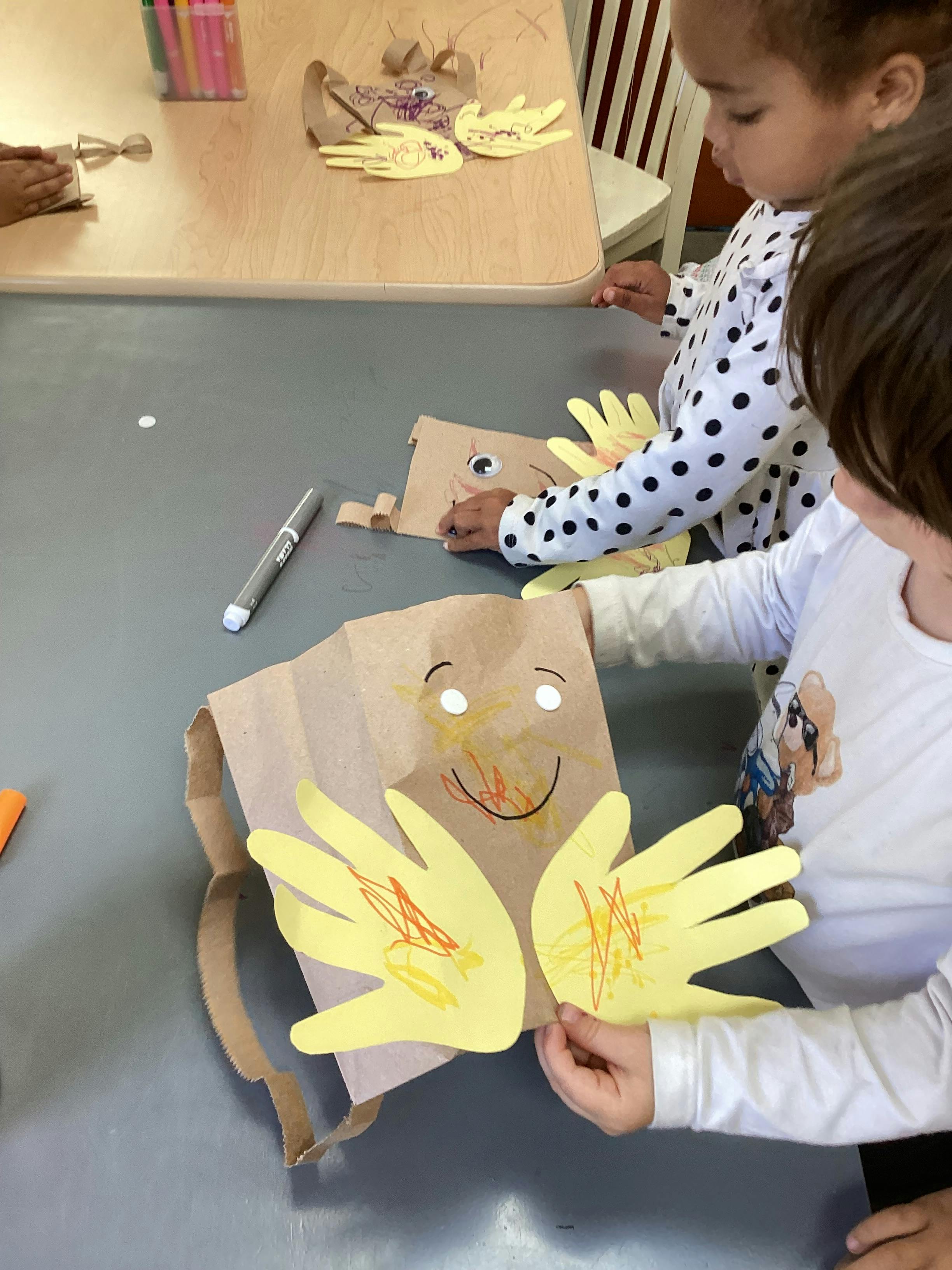 Children making paper bag puppets with paper hand cutouts