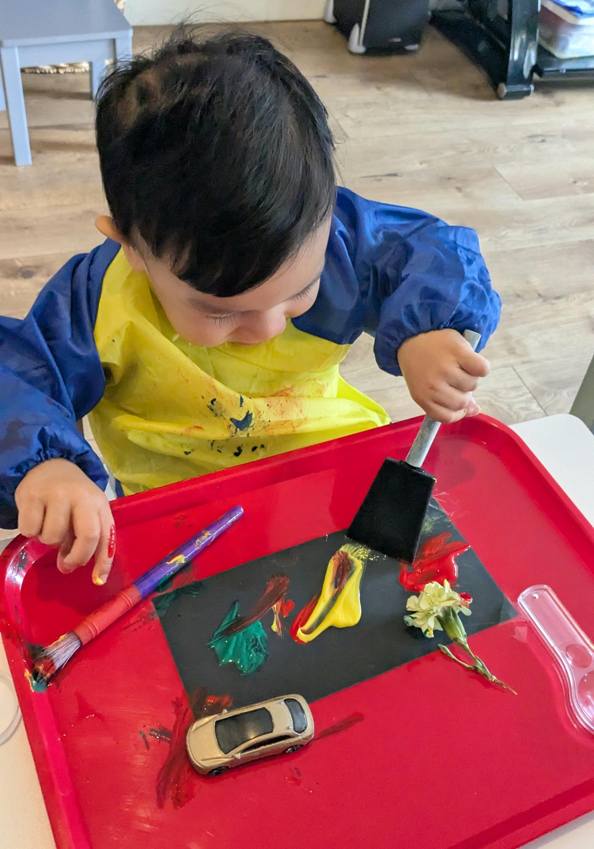 Child in smock painting on black paper with various tools