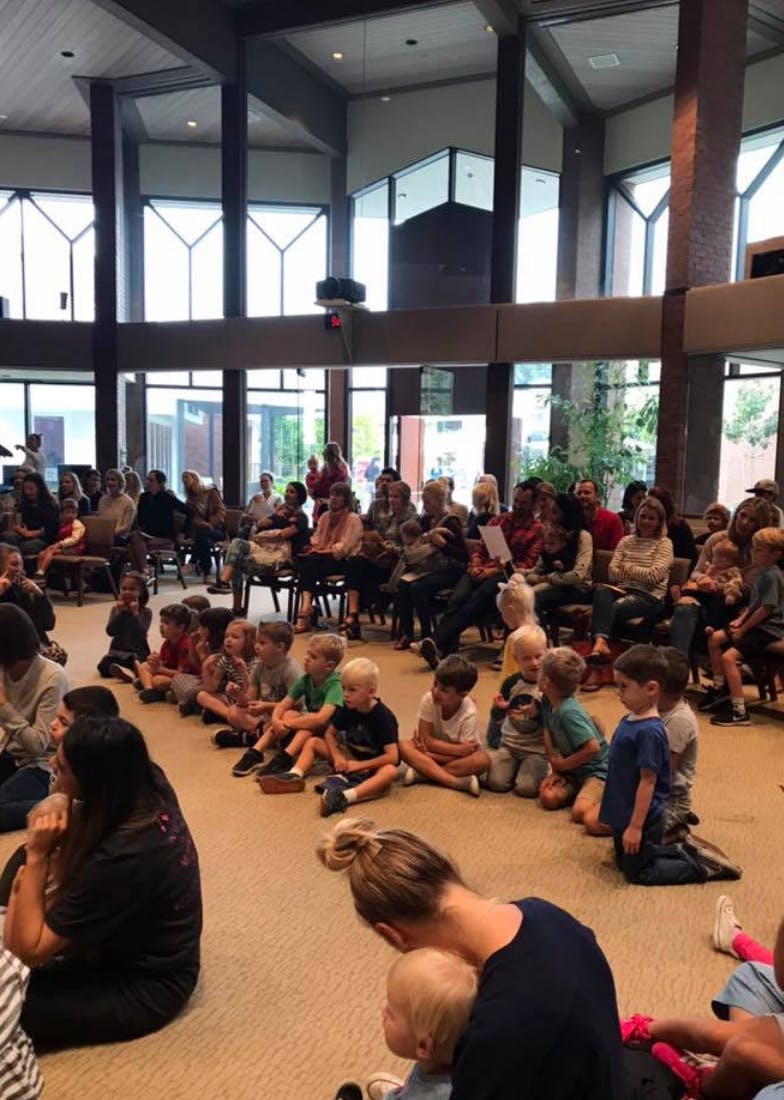 Adults and children sitting on the floor and in chairs in a large room